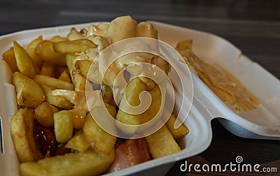 Closeupof French fries and currywurst covered with dip in a to go box Stock Photo