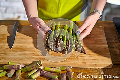 Closue-up image of woman holding a bunch of green asparagus in the kitchen. Cooking at home Stock Photo