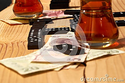 Closup of Dominoes on a grained wooden board, with glasses of black tea and two stacks of Turkish paper money and spare stones Stock Photo