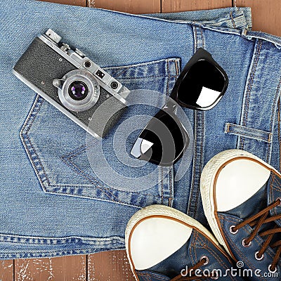 Clothes, shoes and accessories - Top view retro camera, sunglasses, gumshoes and blue jeans on wooden background Stock Photo