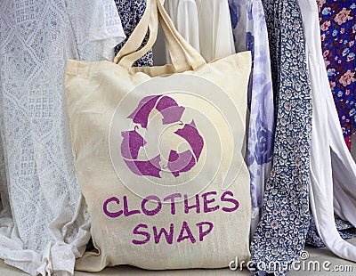 Clothes swap reusable bag with recycle textiles symbol in front of rack of clothes. Recycle clothes for sustainable living Stock Photo