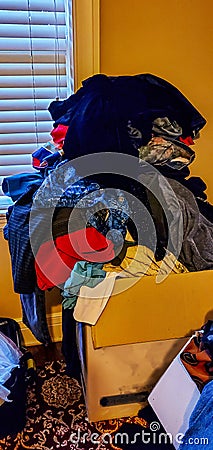 Clothes thrown haphazardly mounded up on moving box by window Stock Photo