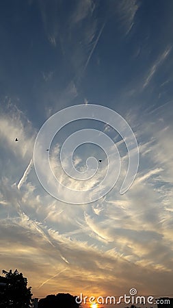 Sun setting in beautifully patterned clouds having traces of airplane path Stock Photo