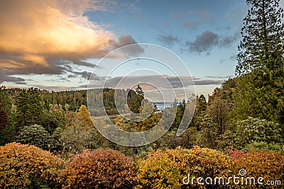 Clouds start to turn orange at sunset looking out over the calm water and bright fall colors near Stonefield Castle in Argyll Stock Photo