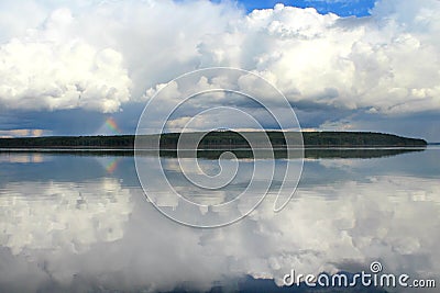 Clouds white on blue sky with a small rainbow with reflection in lake during the day in the natural environtent. Stock Photo