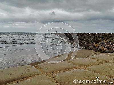 Cloudy day at the beach with dolos heading off into horizon along pier Stock Photo