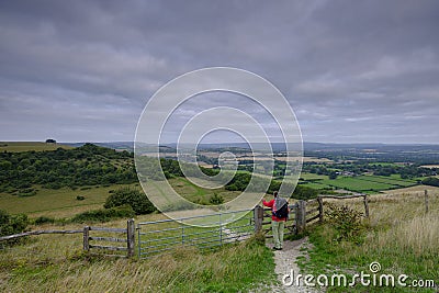 Cloudy overcast summer sunrise over the South Downs Way footpath from A middle aged male walker with backpack admiring the view Stock Photo