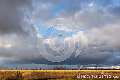 Cloudy sky before a thunderstorm, a field with a road going into the distance. Residential buildings near the horizon Stock Photo