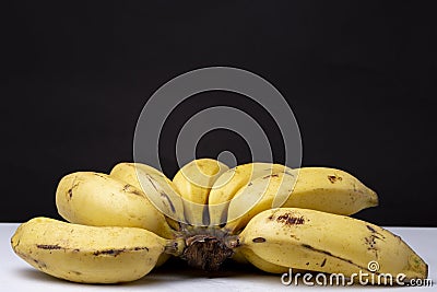 Clsoeup shot of a bunch of ripe yellow bananas on a white surface with a black background Stock Photo