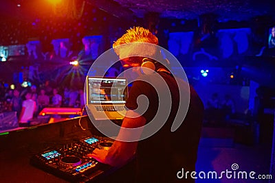 Club, disco DJ playing and mixing music for crowd of happy people. Nightlife, concert lights, flares. Stock Photo