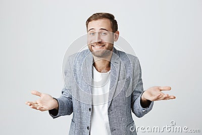 Clueless puzzled attractive man with beard, smiling broadly, having hesitation shrugging shoulders expressing Stock Photo