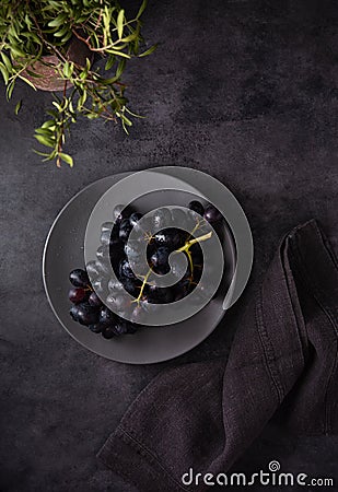 A cluster of juicy black grapes lies in a gray plate with gray napkin on a dark gray table Stock Photo