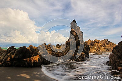 CLUSTERS OF ROCKS ADORN THE BEACH WITH BLUE SKIES AND LUMPY CLOUDS CREATING A BEAUTIFUL VIEW Stock Photo