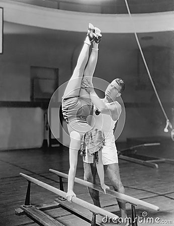 Coach helping woman on parallel bars Stock Photo