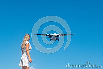 Coastal Encounter: Girl in White Dress on Stones, Plane in Blue Skies Stock Photo