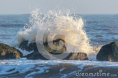 Coastal erosion. Wave crashing against sea flood defence rocks Stock Photo