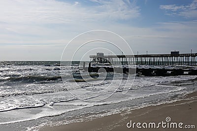 Coastal landscape showing the sandy beach, rough ocean and a pier and wooden jetty extending into the ocean Stock Photo