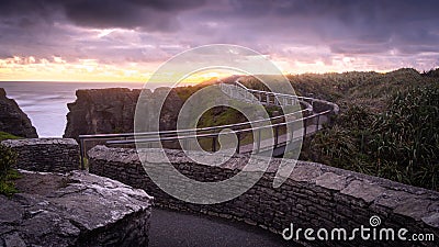 Coastal walkaway leading to horizon with dramatic and cloudy colorful sunset , New Zealand Stock Photo