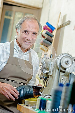 Cobbler holding shoe stood next to sewing machine Stock Photo