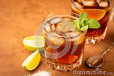 Cocktail of rum and cola ice cubes and lime in a glass goblet on a dark brown background. Strong alcoholic drink. Stock Photo