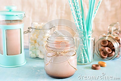 Cocoa in a jar. In the background, a turquoise coffee pot, marshmallows and blue cocktail tubes in a blur. A gentle Stock Photo
