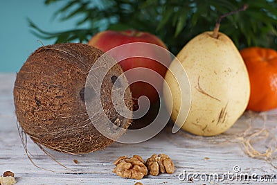 Coconut, pear, apple, tangerine and walnuts on a white wooden table next to a palm tree Stock Photo