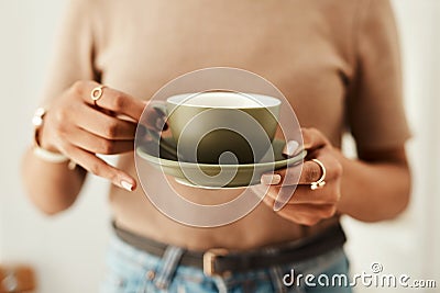 Coffee anyone. an unrecognizable woman standing alone in her home and holding a cup of coffee. Stock Photo