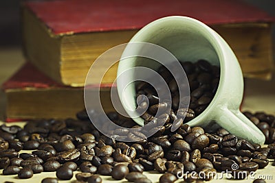 Coffee bean in tilted ceramic cup and old book laid behind. Stock Photo