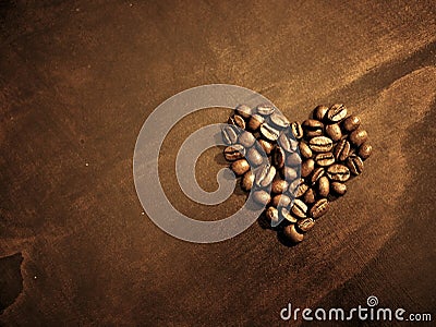 Coffee beans at breakfast shaped in heart on wood grain background. Stock Photo