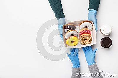 Coffee break for lunch during covid-19 pandemic. Customer in rubber gloves takes a box of glazed donuts and two cups of Stock Photo