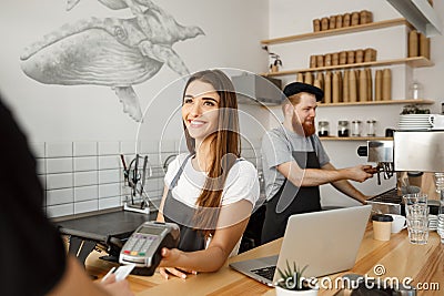 Coffee business concept - beautiful female barista giving payment service for customer with credit card and smiling Stock Photo