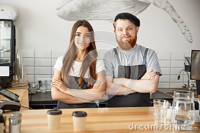 Coffee Business Concept - Positive young bearded man and beautiful attractive lady barista couple in apron looking at Stock Photo