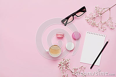 Coffee, cake macaron, notebook, eyeglasses and flower on pink table from above. Female working desk. Cozy breakfast. Flat lay. Stock Photo