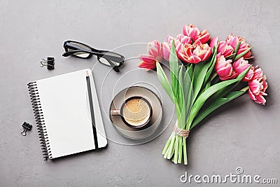 Coffee, clean notebook, eyeglasses and beautiful tulip flower on stone table top view in flat lay style. Woman working desk. Stock Photo