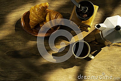 Coffee cup with a croissant and fresh coffee beans on an old wooden floor while camping in the forest Stock Photo