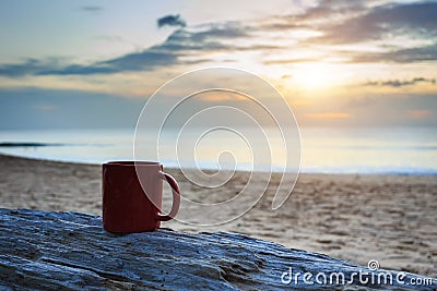 Coffee cup on wood log at sunset or sunrise beach Stock Photo