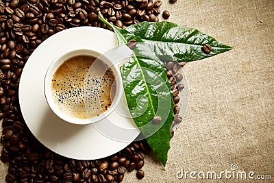 Coffee with foam cup with beans on the left with green leaf on flax Stock Photo