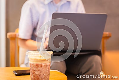 Coffee Frappuccino Blended with paper straw and woman using laptop in background. Stock Photo