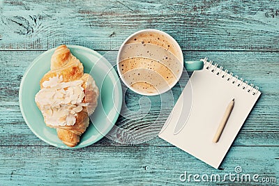 Coffee mug with croissant and empty notebook and pencil for business plan and design ideas on turquoise rustic table from above Stock Photo