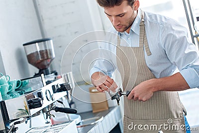 Coffee Passion. Young barista at coffee shop cleaning portafilter pensive close-up Stock Photo