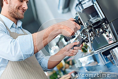 Coffee Passion. Young barista at coffee shop inserting portafilter into espresso machine close-up smiling cheerful Stock Photo