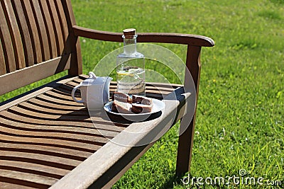 Coffee pitcher, glass bottle of homemade lemonade and cake on wooden bench, blurred green grass background. Outdoor Stock Photo