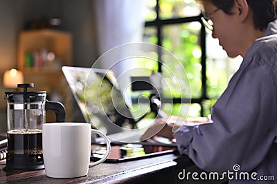 A coffee press and a cup on a work desk with a person working from home Stock Photo