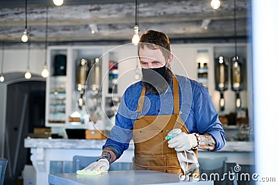Coffee shop man owner working with face mask and gloves, disinfecting tables. Stock Photo
