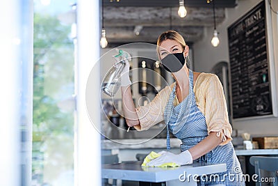 Coffee shop woman owner working with face mask and gloves , disinfecting tables. Stock Photo