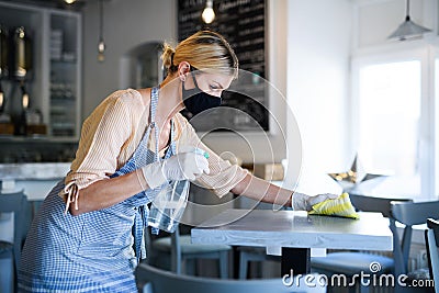 Coffee shop woman owner working with face mask and gloves, disinfecting tables. Stock Photo