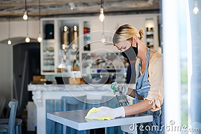 Coffee shop woman owner working with face mask and gloves, disinfecting tables. Stock Photo