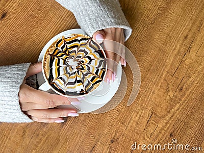 Coffee with spider web pattern on top of foam in white cup and girl& x27;s hands on wooden table background Stock Photo