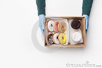 Coffee with sweets for two takeaway during covid outbreak. Waiter in rubber gloves gives box of donuts with glaze and Stock Photo