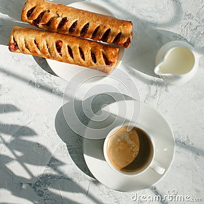 Coffee white cup, sweet rools and milk on gray background in sunlight ray, selective focus. Breakfast concept, shadow, copy space Stock Photo